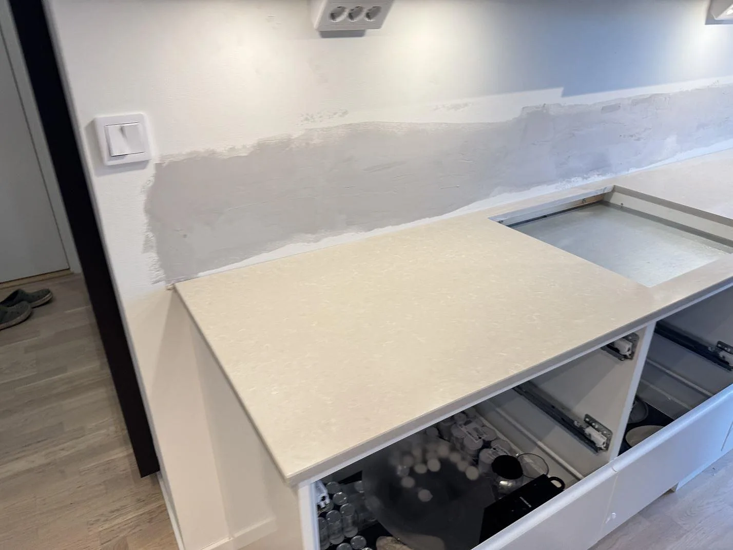 Väggbänk i polerad Technistone Noble Ivory White med låg stänkkant och ljus köksinredning under montering i Malmö.