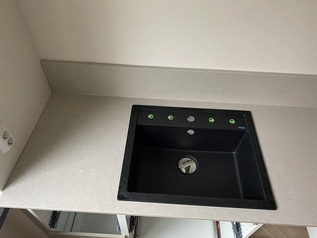 Närbild på polerad Technistone Noble Ivory White i kvartskomposit med svart diskho och uppvikt stänkkant i ett kök i Malmö.