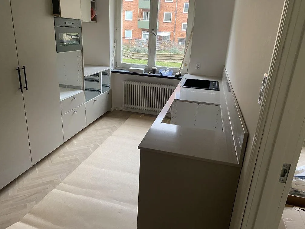Översiktsbild av ett smalt kök i Malmö med polerad Technistone Noble Ivory White som ljus bänkskiva längs väggen under montering.
