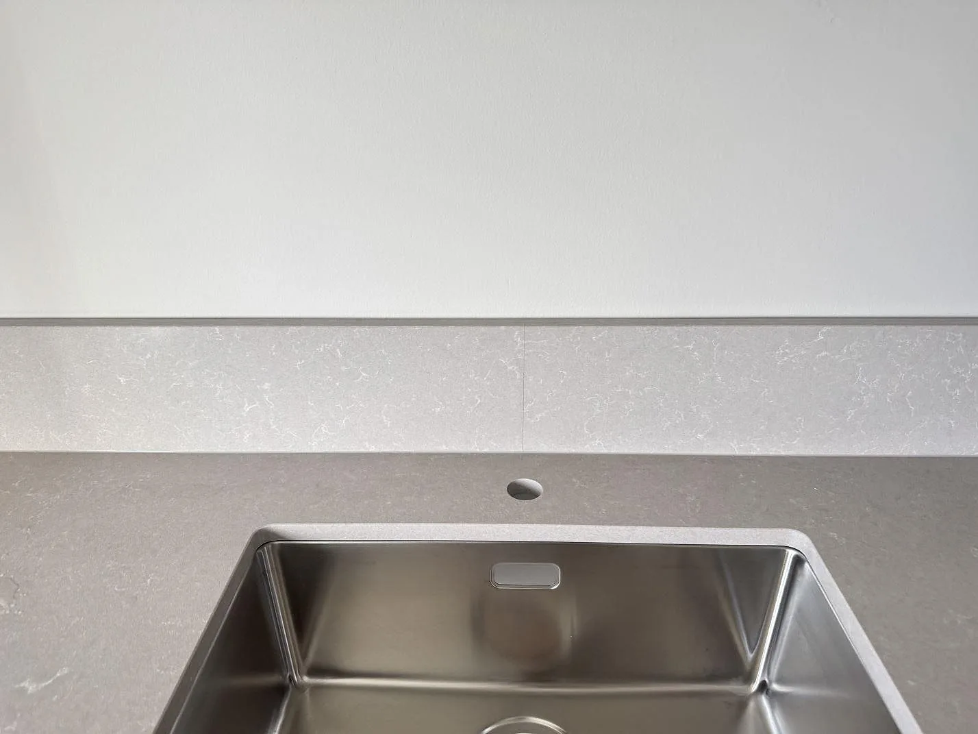 Detalj av stänkskydd och diskho i en polerad Technistone Noble Ivory White köksbänkskiva i Malmö.