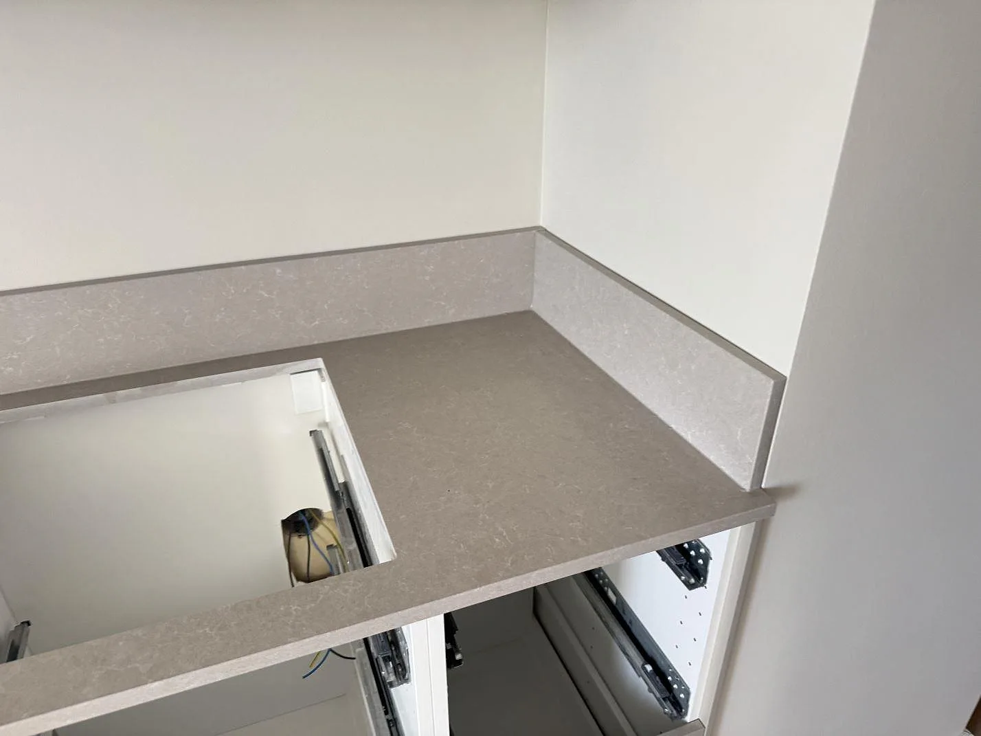 Hörnparti med köksbänkskiva och stänkskydd i polerad Technistone Noble Ivory White under montering i Malmö.