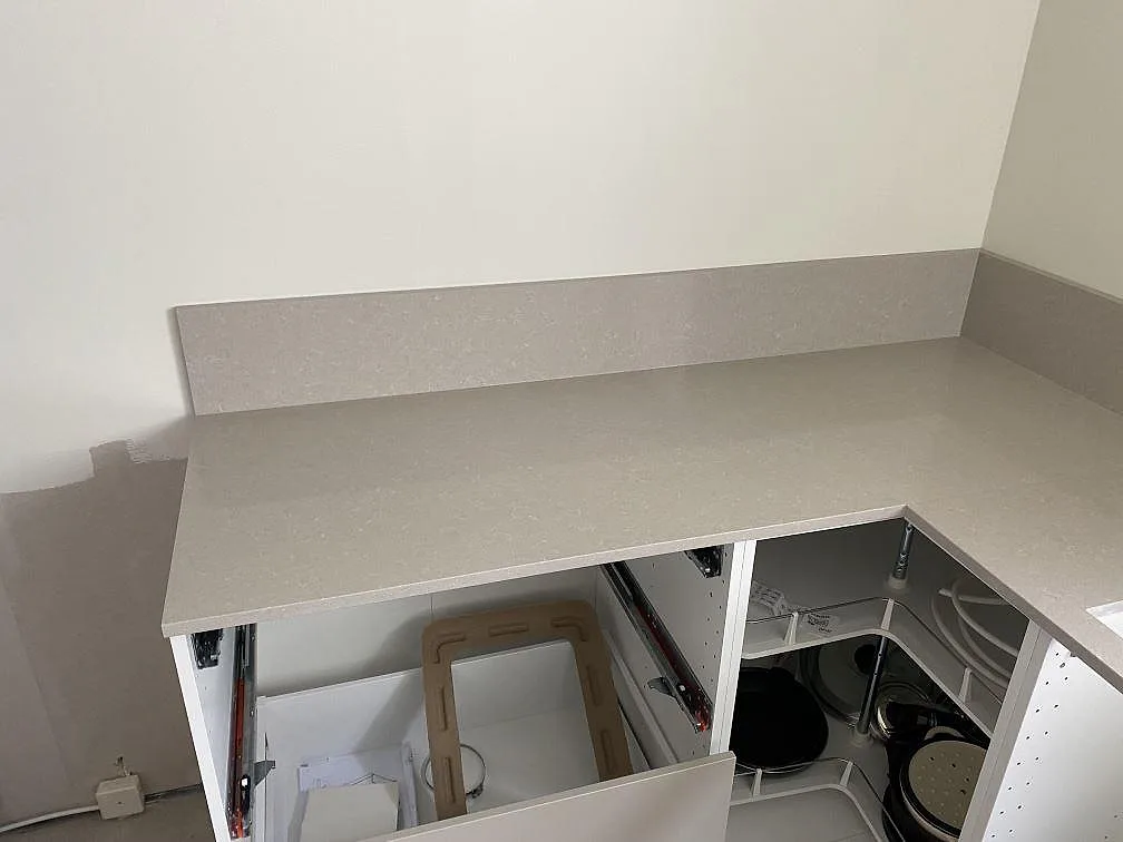 Hörn av U-formad köksbänkskiva i Technistone Noble Ivory White, polerad ljus kvartskomposit med stänkkant under montering i Malmö.