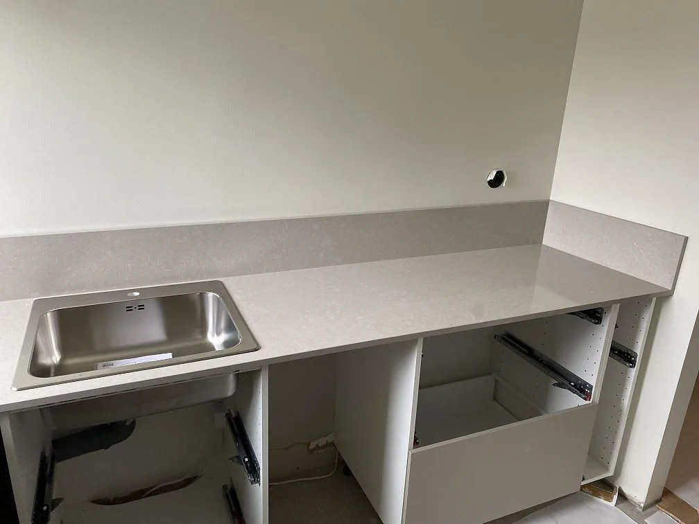 Polerad köksbänkskiva i Technistone Noble Ivory White med rostfri diskho och uppvikt stänkkant i ett kök under montering i Malmö.