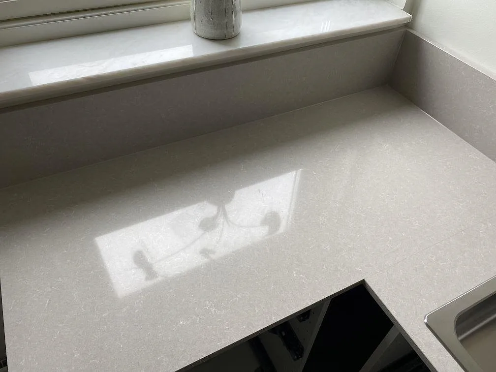 Närbild på polerad Technistone Noble Ivory White med fönsterreflektion, låg stänkkant och synlig diskhokant i ett kök i Malmö.