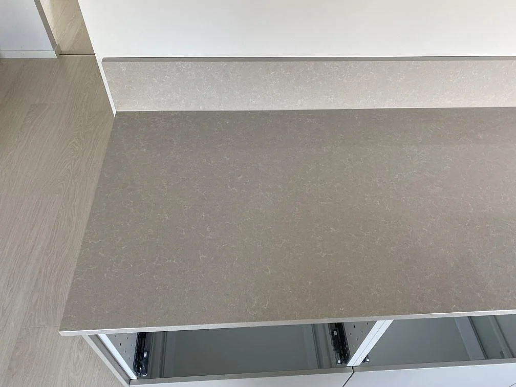 Närbild på polerad Technistone Noble Ivory White kvartskomposit med låg stänkkant och öppen köksstomme i Malmö.