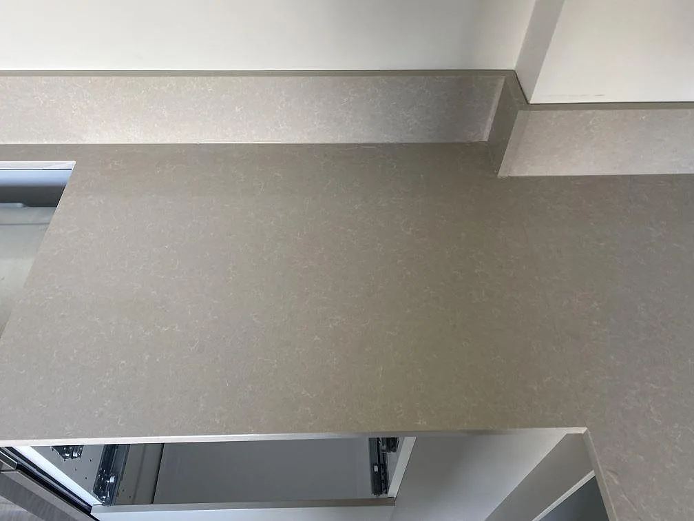 Installerad arbetsyta i polerad Technistone Noble Ivory White kvartskomposit med stänkkant och synligt hälluttag i Malmö.