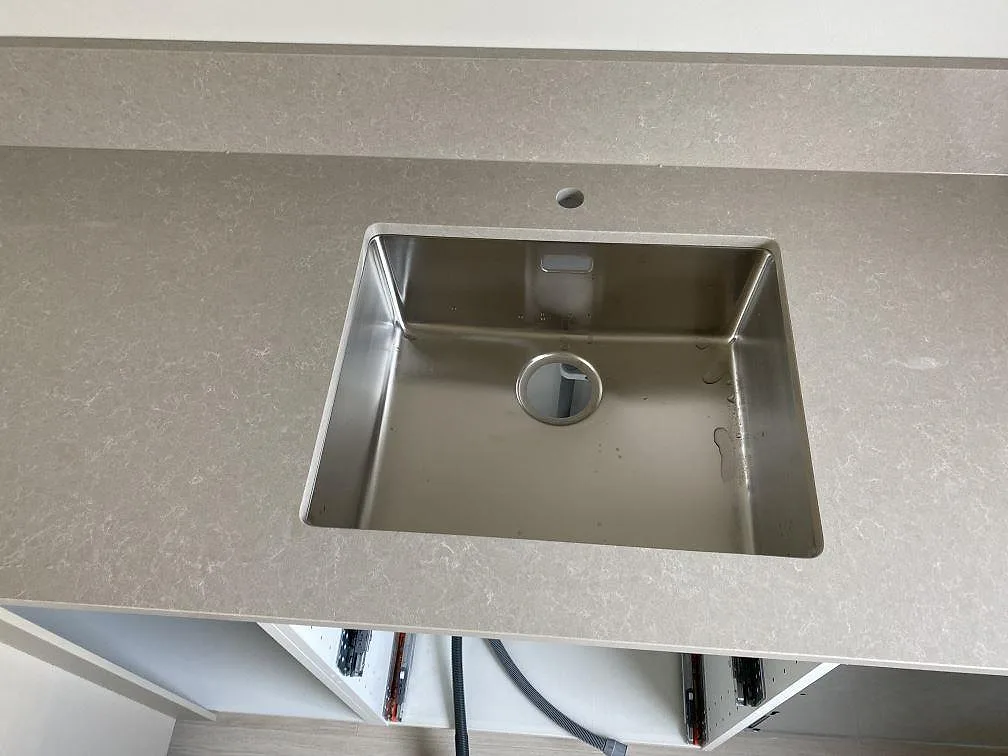 Diskhozon i polerad Technistone Noble Ivory White kvartskomposit med rostfri diskho och låg stänkkant i ett kök i Malmö.