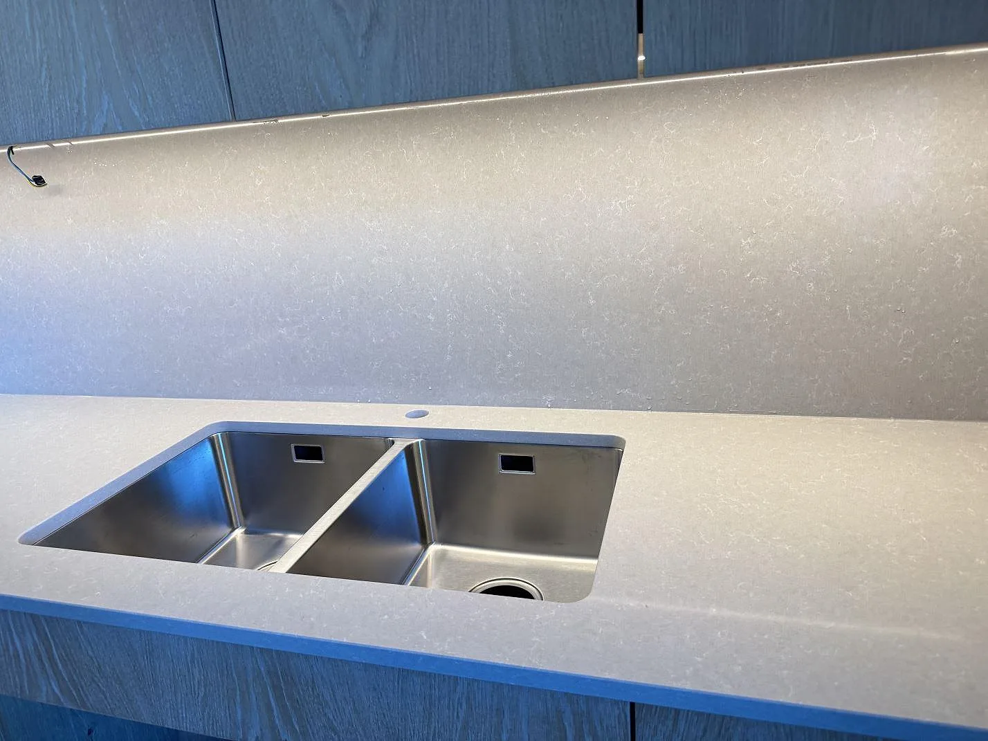 Detalj av polerad Technistone Noble Ivory White komposit runt rostfri dubbelho och stänkpanel under väggskåp i kök i Malmö.