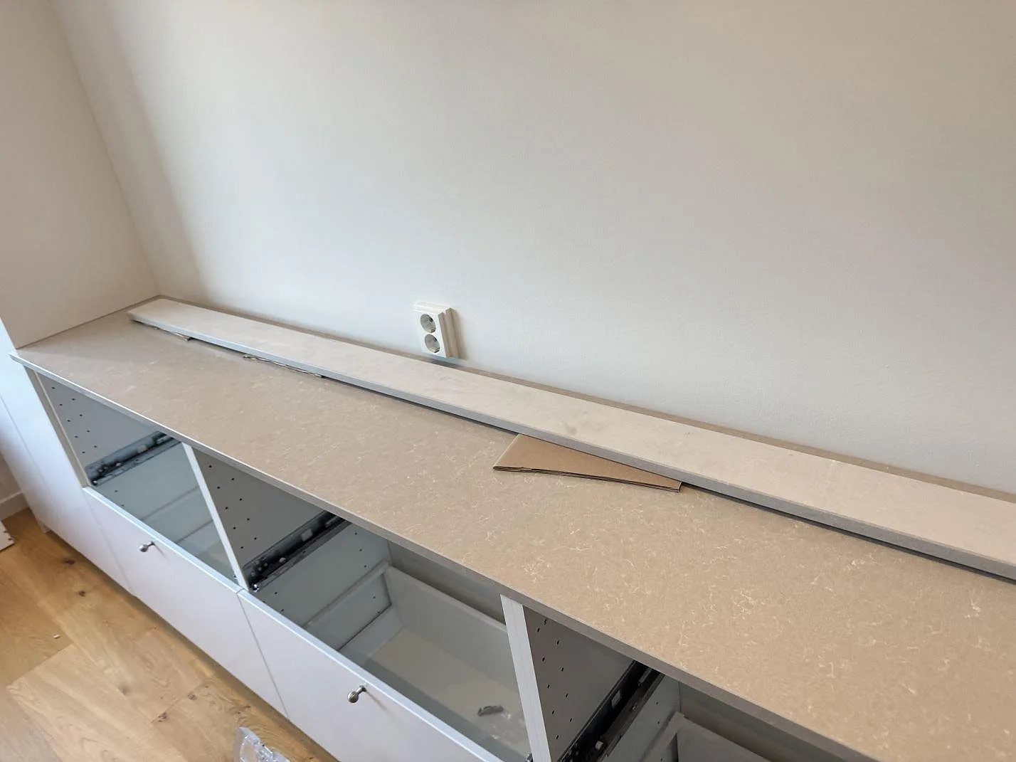 Lång köksbänk i polerad Technistone Noble Ivory White komposit på vita stommar med lös stenlist under montering i Malmö.