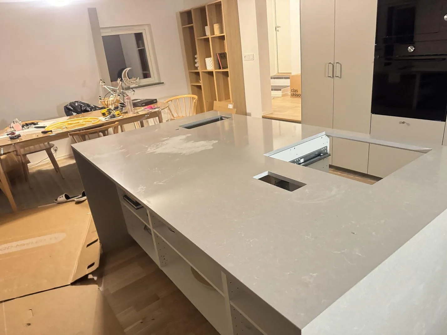 Stor köksö i polerad Technistone Noble Ivory White, vit kvartskomposit, i ett öppet kök under montering i Malmö, med urtagningar för häll och inbyggnadsenhet.