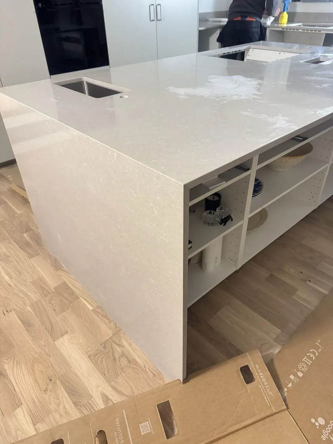 Blank, polerad yta på köksö i Technistone Noble Ivory White komposit med öppen förvaring och liten rostfri preppho i ett kök i Malmö.