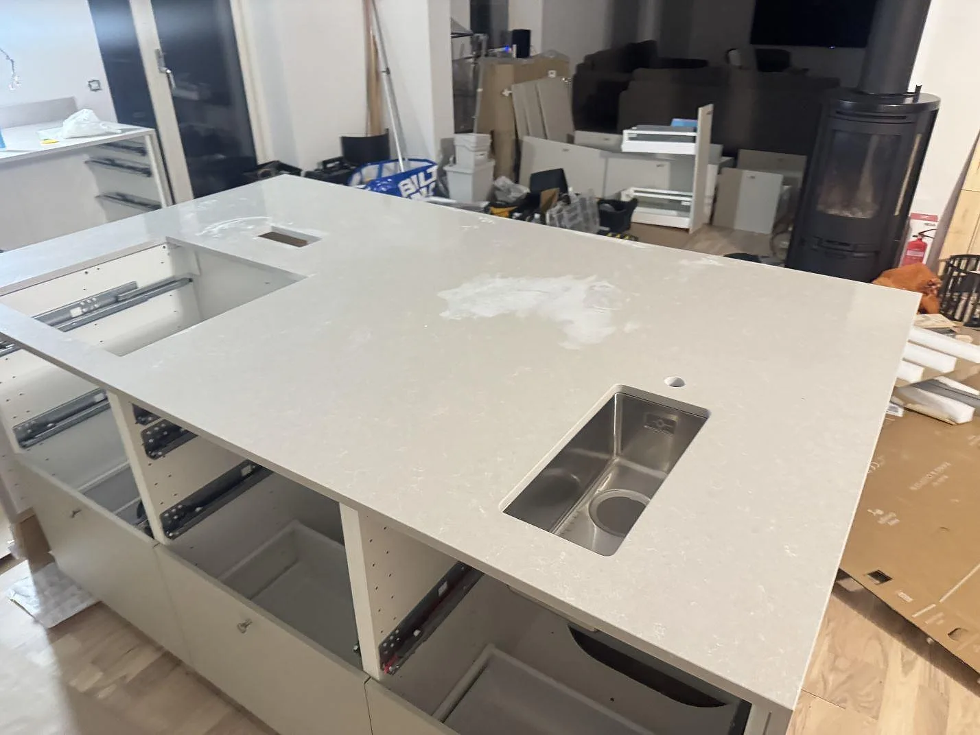 Köksö i vit Technistone Noble Ivory White, polerad komposit, med liten underlimmad rostfri preppho och fristående kaminkassett i ett kök i Malmö.