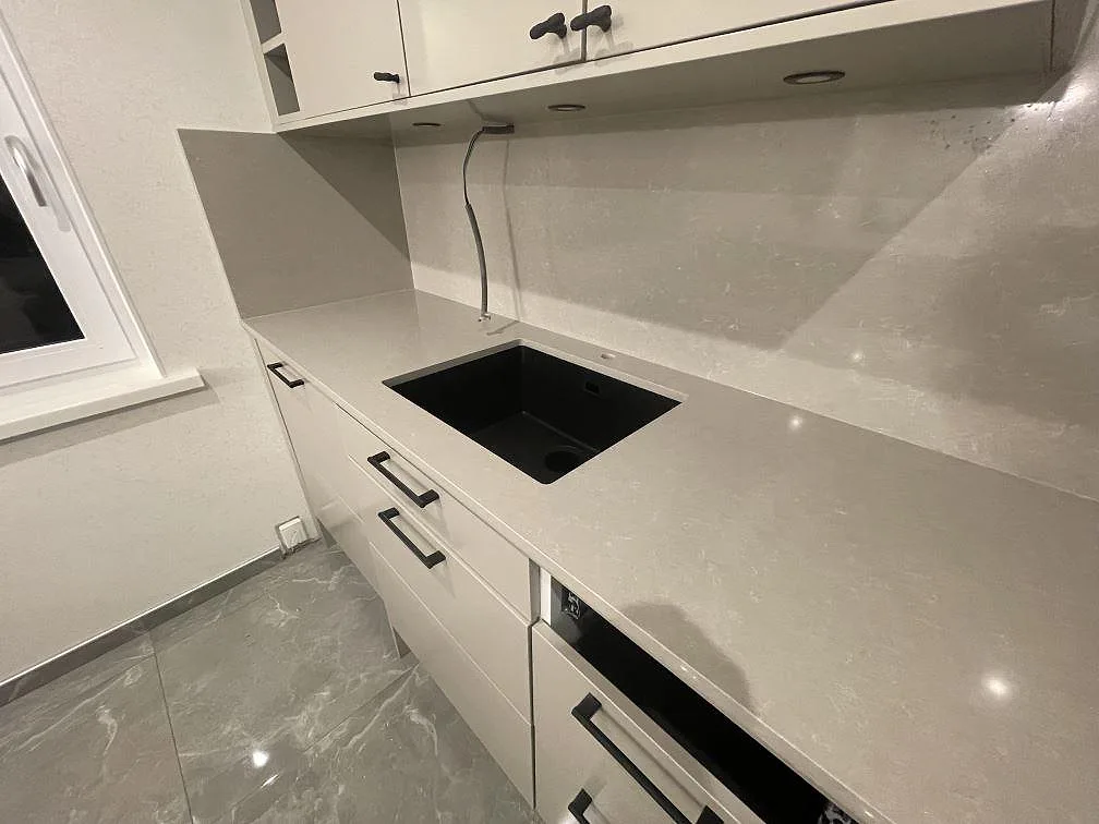 Polerad bänkskiva i Technistone Noble Ivory White med svart underlimmad komposithoar och stänkskydd i samma ljusa sten i ett kök i Norrköping.