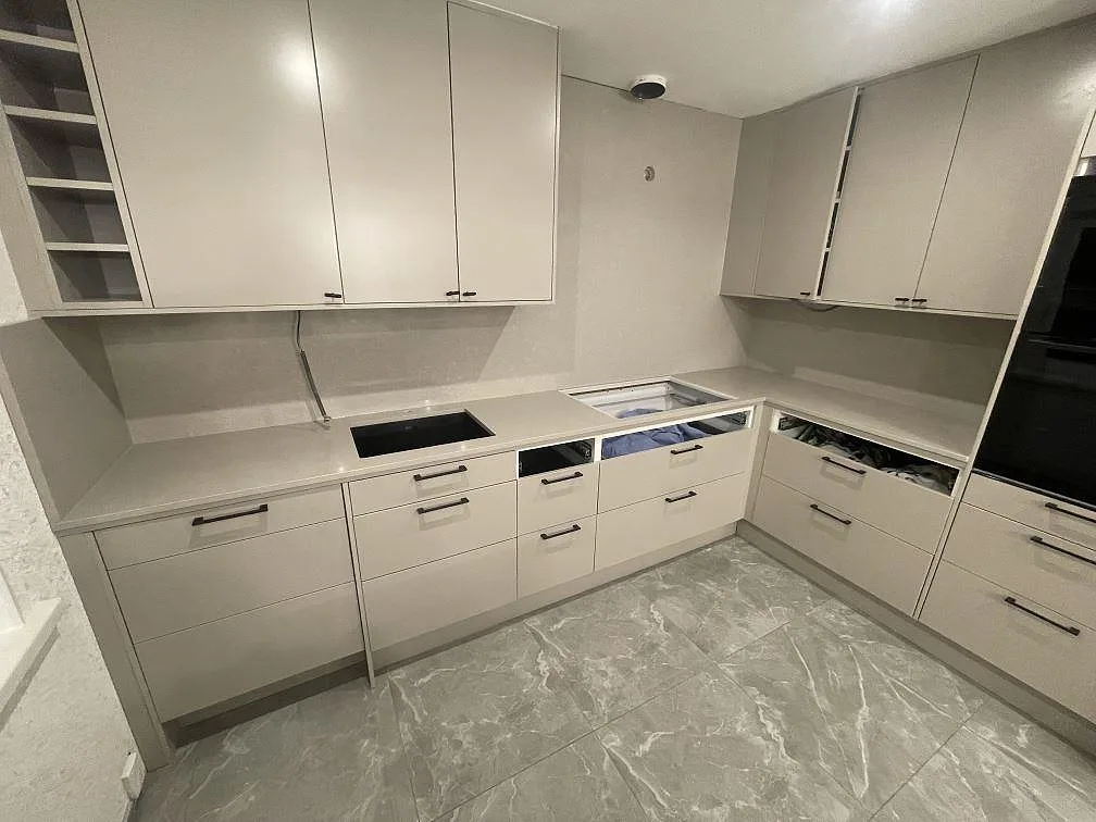 Köksbänkskiva i elfenbensvit Technistone Noble Ivory White längs L-raden med stänkskydd och urtag för induktionshäll under montering i Norrköping.