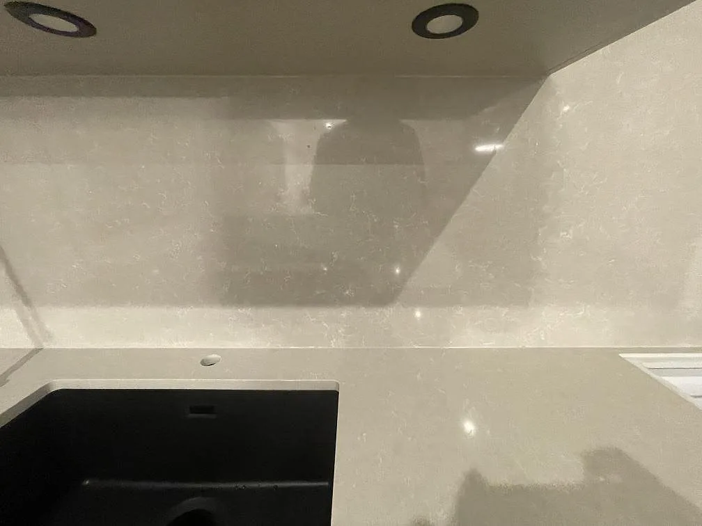 Detalj av svart underlimmad komposithoar i polerad Technistone Noble Ivory White med spräcklig ådring och högt stänkskydd i ett kök i Norrköping.