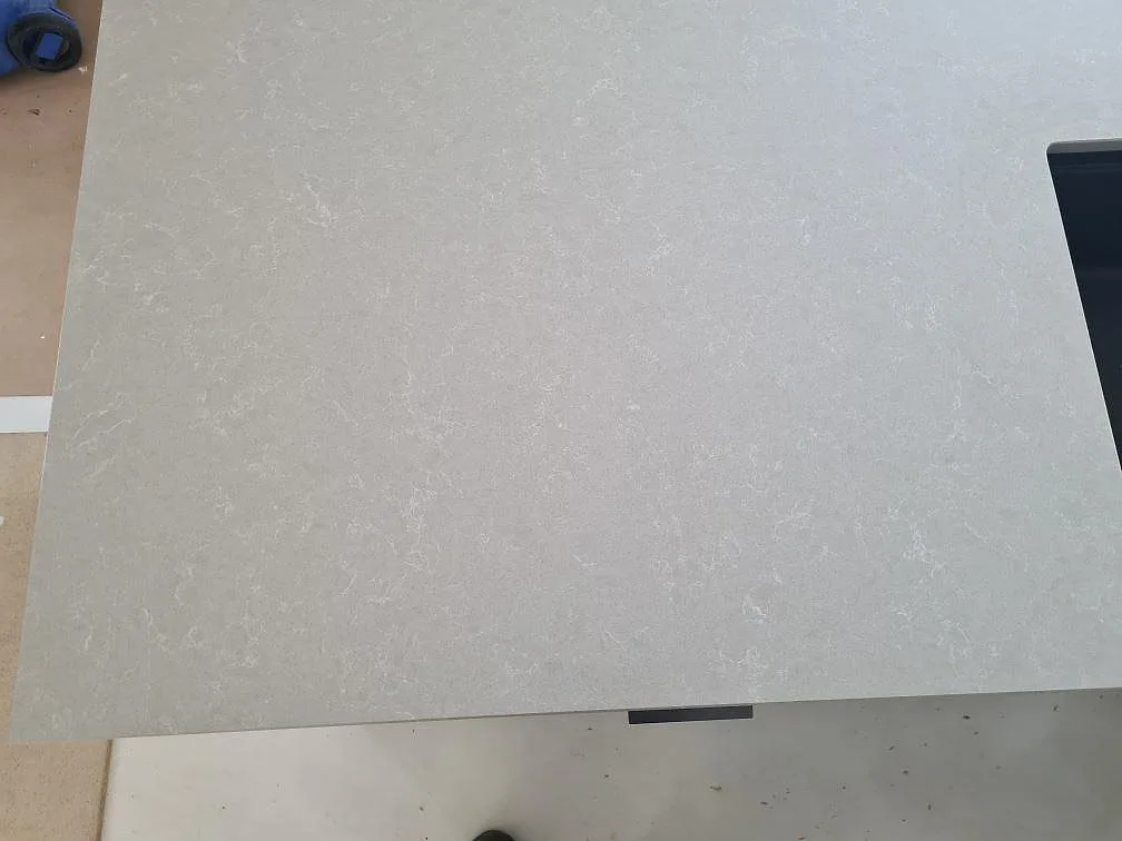 Närbild av ljus polerad Technistone Noble Ivory White kvartskomposit på köksbänk med hällkant synlig i Ösmo.