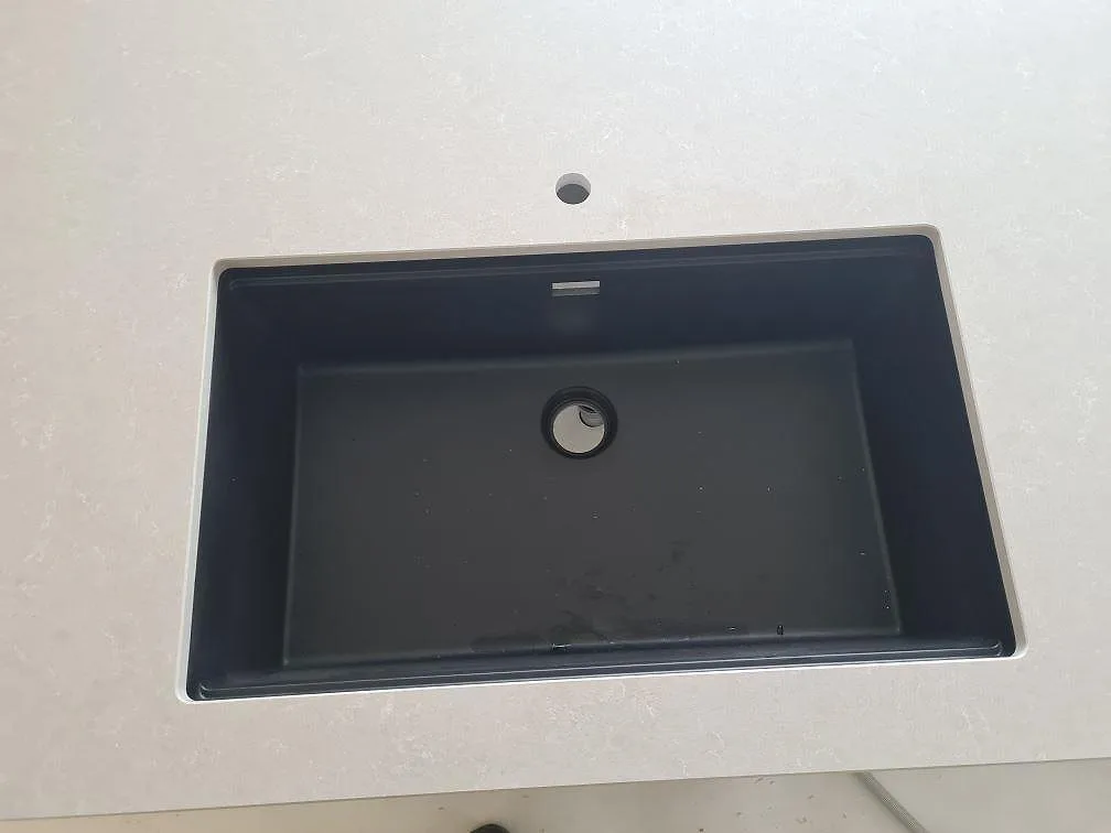 Detalj av svart underlimmad diskho i en polerad Technistone Noble Ivory White bänkskiva i ett kök i Ösmo.