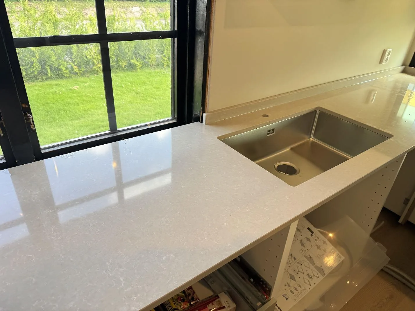 Köksbänkskiva i Technistone Noble Ivory White, 20 mm polerad kvartskomposit, med rostfri diskho och låg stänkkant vid fönster i Oskarström.