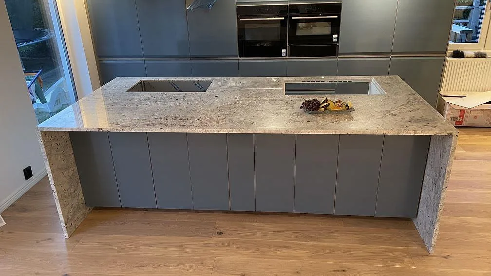 Köksö med bänkskiva i Technistone Noble Ivory White, 20 mm polerad kvartskomposit, med häll och diskho i ett kök i Oskarström.
