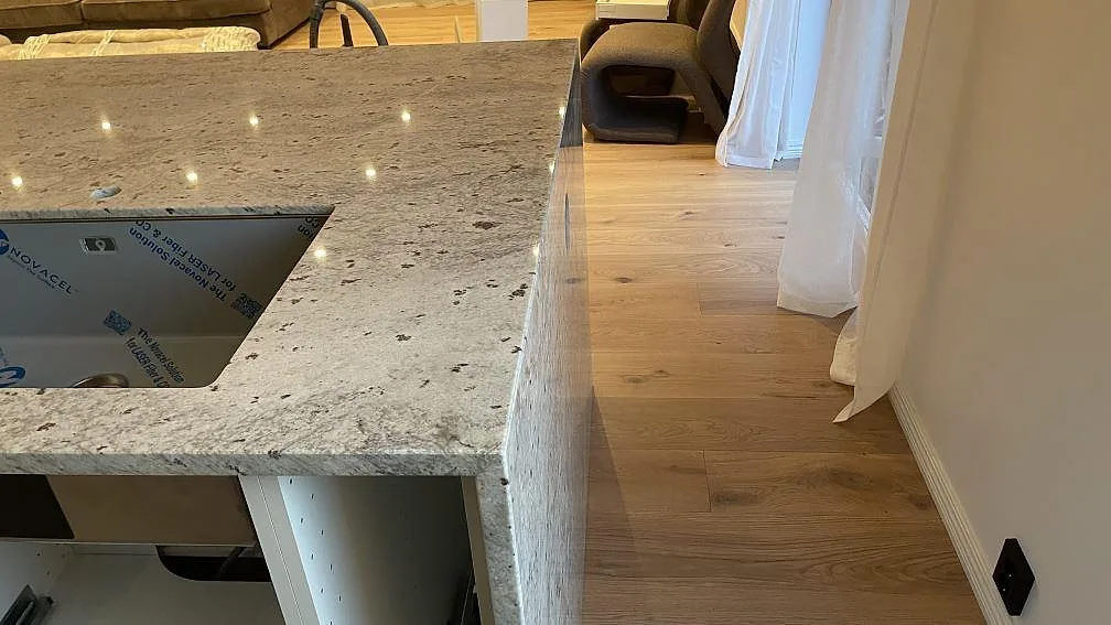 Kant och neddragen sida på köksö i polerad Technistone Noble Ivory White med synlig ådring i Oskarström.