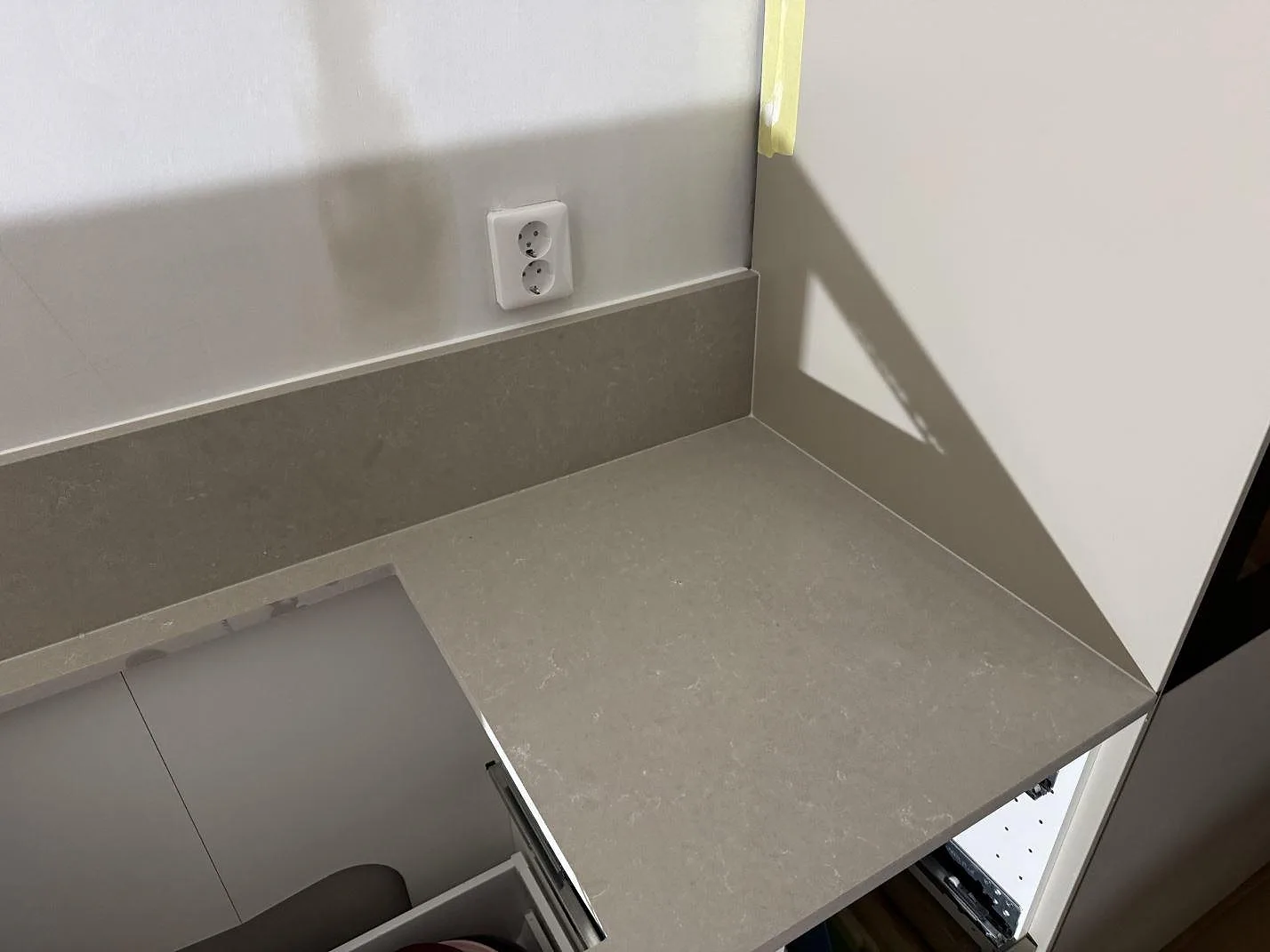 Sidodel av köksbänkskiva i polerad Technistone Noble Ivory White med uppvikt stänkkant och vägguttag i Ronneby.