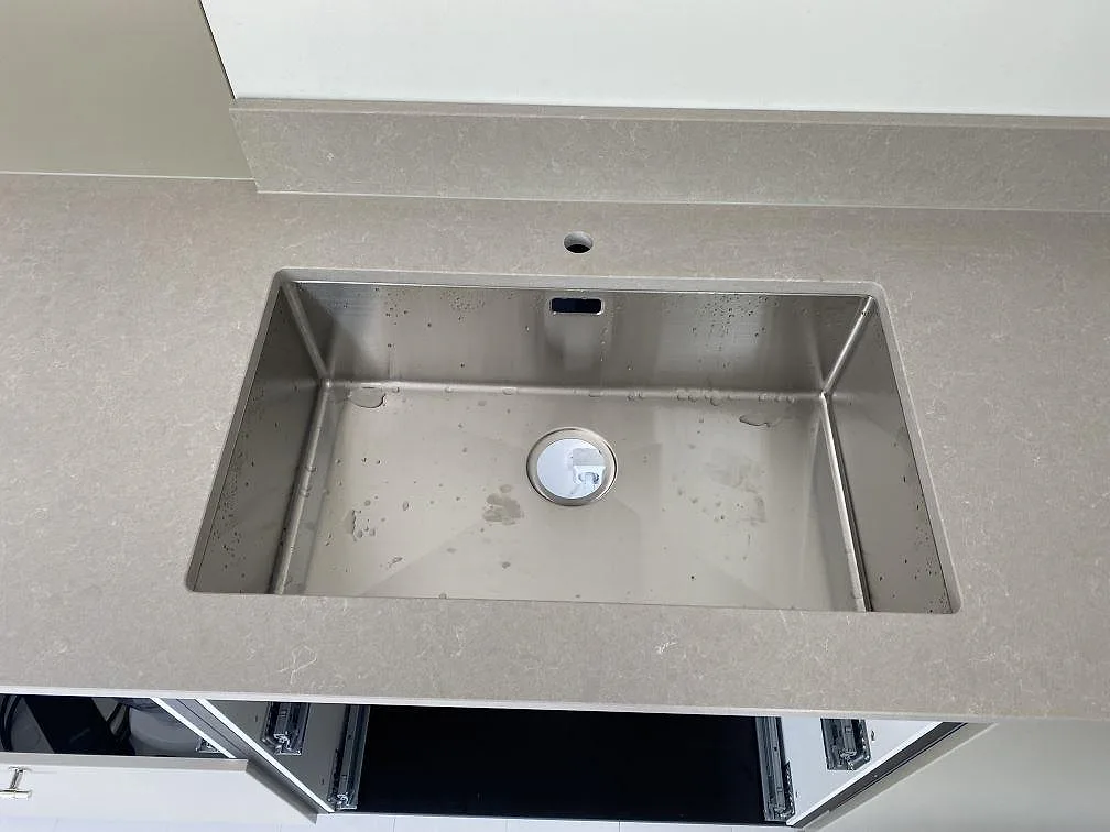 Närbild på rostfri diskho i bänkskiva av polerad Technistone Noble Ivory White komposit med stänkkant i Simrishamn.