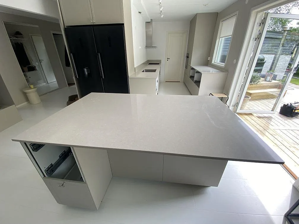 Köksbänkskiva och köksö i polerad Technistone Noble Ivory White, vit komposit, i ett kök i Simrishamn.