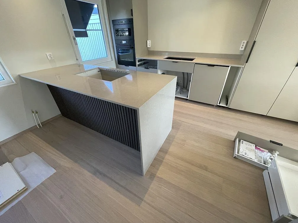 Köksbänkskiva i polerad Technistone Noble Ivory White, kvartskomposit, med köksö och bänkar längs vägg i Skutskär.
