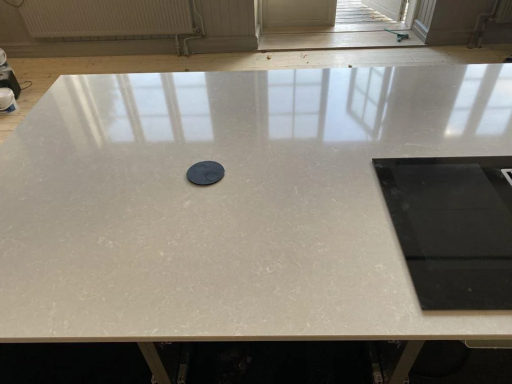 Köksö i polerad Technistone Noble Ivory White med induktionshäll och speglande yta i ett kök i Staffanstorp.