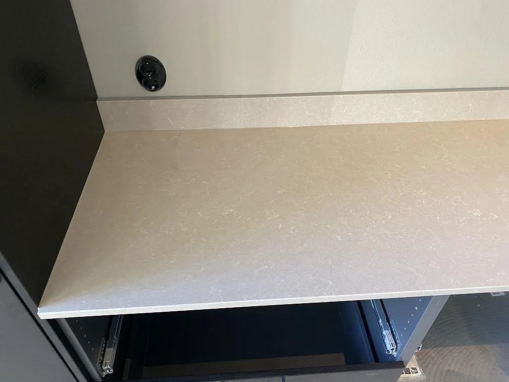 Bänkskiva i varmvit Technistone Noble Ivory White med uppvikt stänkskydd i samma sten i ett kök i Staffanstorp.