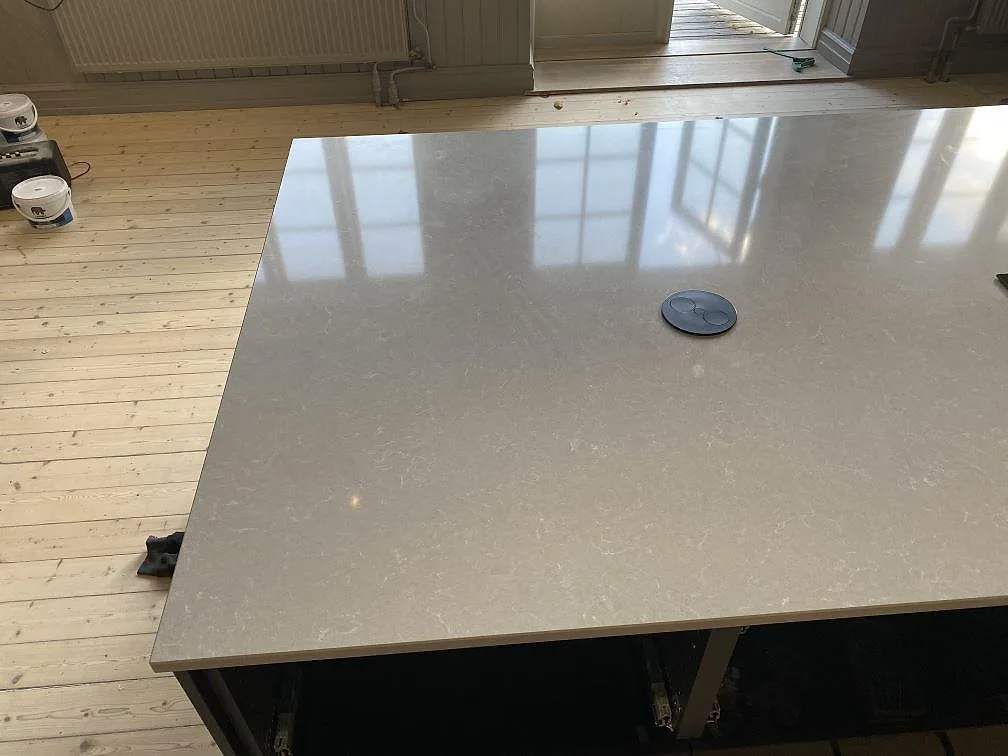 Polerad köksö i Technistone Noble Ivory White med kabelgenomföring och varmvit ådring i ett kök i Staffanstorp.