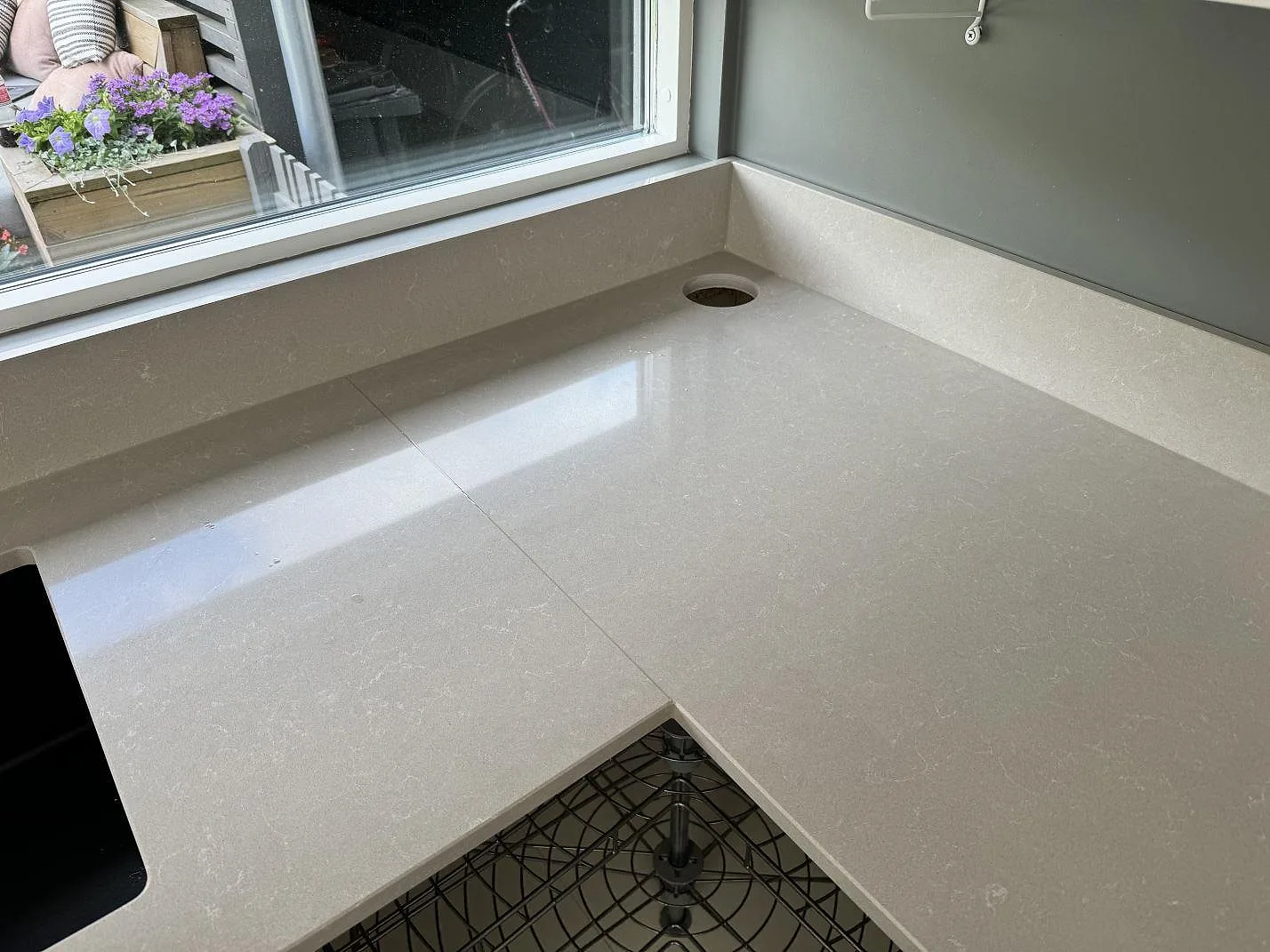 L-formad köksbänkskiva i Technistone Noble Ivory White, polerad kvartskomposit, med uppvikt stänkkant och blandarhål vid fönster i Staffanstorp.
