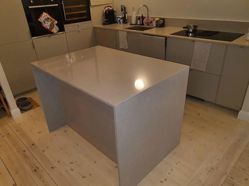 Köksbänkskiva i Technistone Noble Ivory White, polerad varm gråbeige kvartskomposit, med köksö med helstensgavlar, underlimmad diskho och induktionshäll i ett kök i Stockholm.