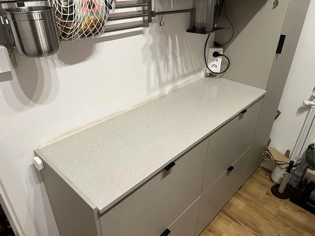 Rak köksbänkskiva i polerad Technistone Noble Ivory White kvartskomposit på skåpsrad med väggförvaring i ett kök i Stockholm.