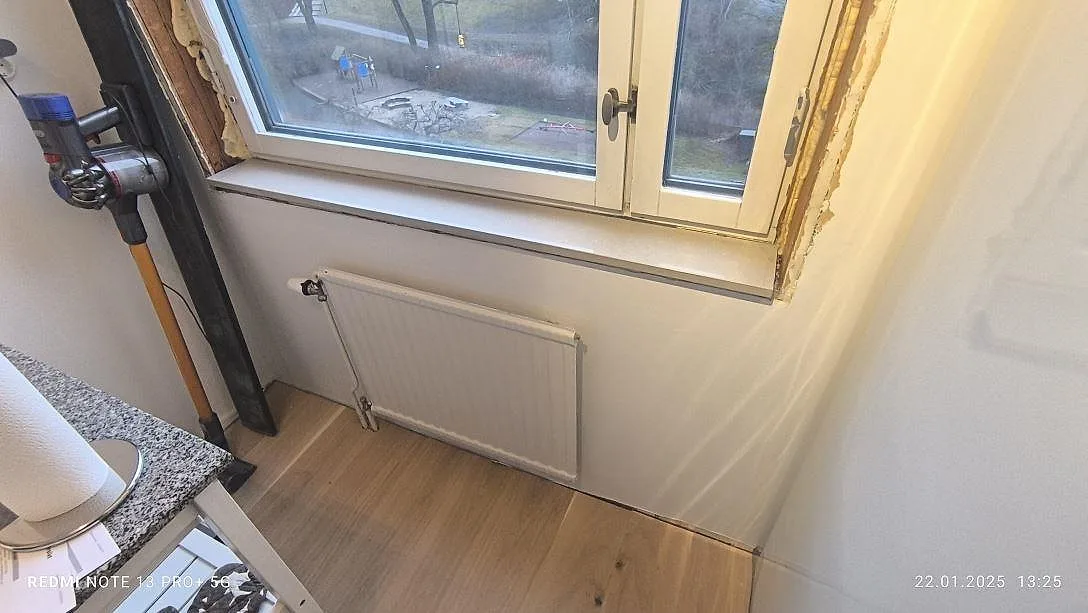 Installerad fönsterbänk i ljus polerad Technistone Noble Ivory White vid köksfönster under pågående montering i Stockholm.