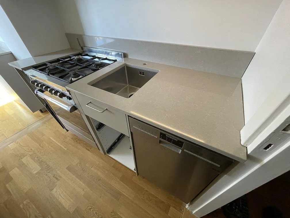 Polerad bänkskiva i Technistone Noble Ivory White med rostfri diskho och uppvikt stänkkant i ett kök i Stockholm.