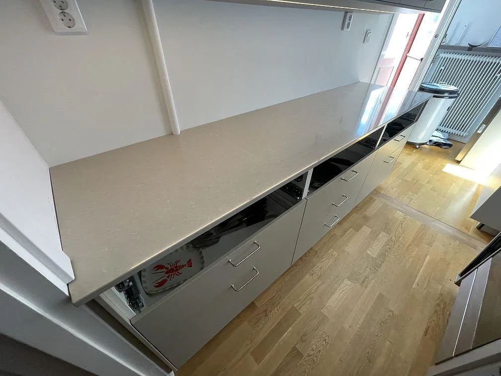 Lång arbetsyta i polerad Technistone Noble Ivory White, kvartskomposit, längs ena sidan av ett smalt Stockholmskök.