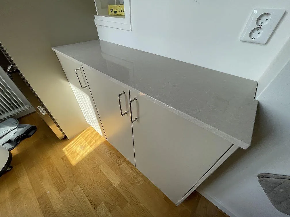 Kort bänkyta i polerad Technistone Noble Ivory White på vit köksinredning vid fönsternisch i Stockholm.