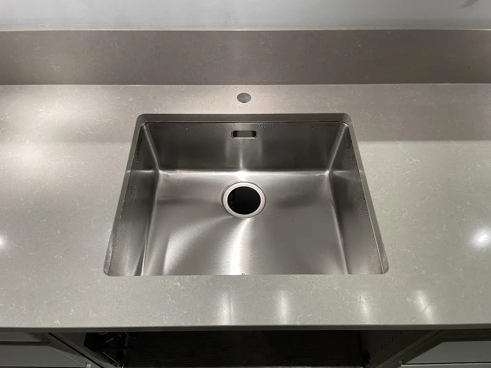 Närbild på rostfri diskho i polerad Technistone Noble Ivory White, kompositbänkskiva med uppvikt stänkkant i Stockholm.