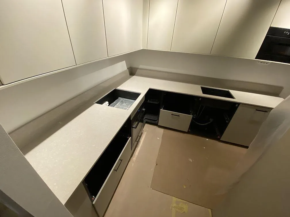 U-format kök i Stockholm med polerad köksbänkskiva i Technistone Noble Ivory White som löper runt väggarna, med urtag för diskho och induktionshäll och öppna stommar under montering.