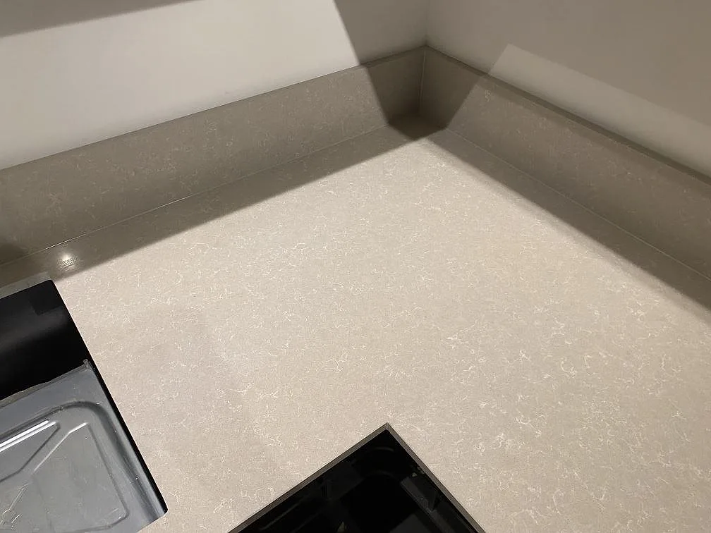 Hörn av köksbänkskiva i Technistone Noble Ivory White med uppvikt stänkkant, polerad yta och mjuk finkornig ådring, i ett kök i Stockholm.