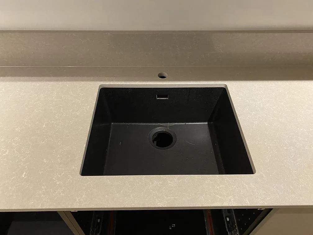 Svart underlimmad kompositdiskho monterad under en polerad köksbänkskiva i Technistone Noble Ivory White, med separat borrat blandarhål, i ett kök i Stockholm.