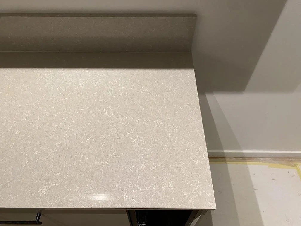 Polerad bänkskiva i Technistone Noble Ivory White med uppvikt stänkkant i samma sten, en varm elfenbensvit komposit med mjuk ådring, i ett kök i Stockholm.