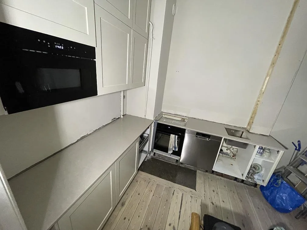 Översikt av ett kök under montering i Stockholm med polerad bänkskiva i Technistone Noble Ivory White längs väggen och öppna köksstommar.