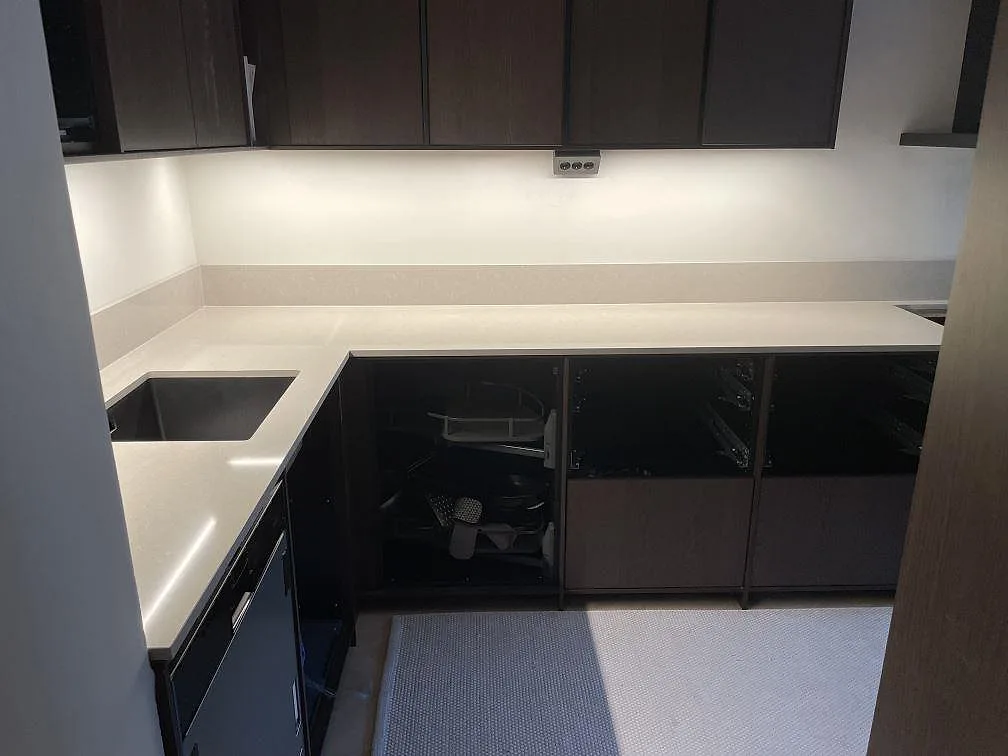 Köksbänkskiva i polerad Technistone Noble Ivory White i en köksvrå med underlimmad diskho och mörka snickerier i ett kök i Stockholm.
