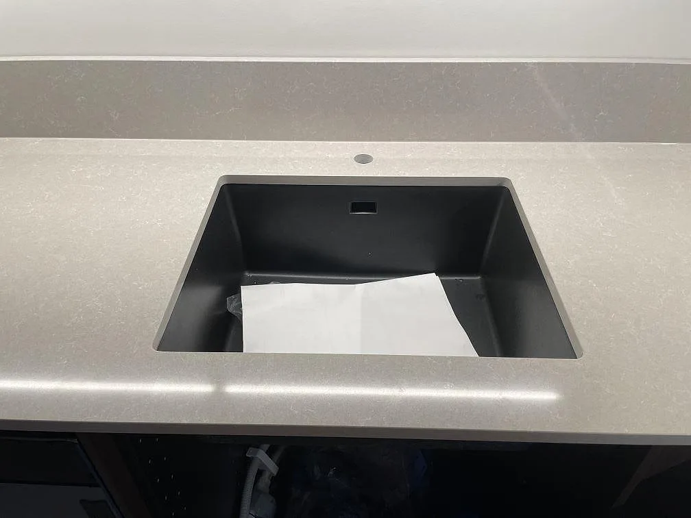Underlimmad mörk diskho med separat blandarhål i en varmvit köksbänkskiva av Technistone Noble Ivory White, polerad kvartskomposit, i ett kök i Stockholm.