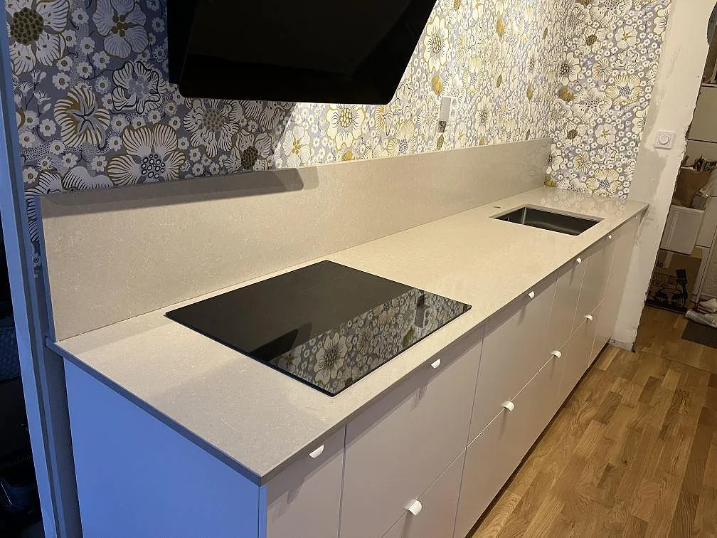 Köksbänkskiva i vit Technistone Noble Ivory White komposit, polerad, med häll, diskho och stänkkant i ett kök i Sundbyberg.