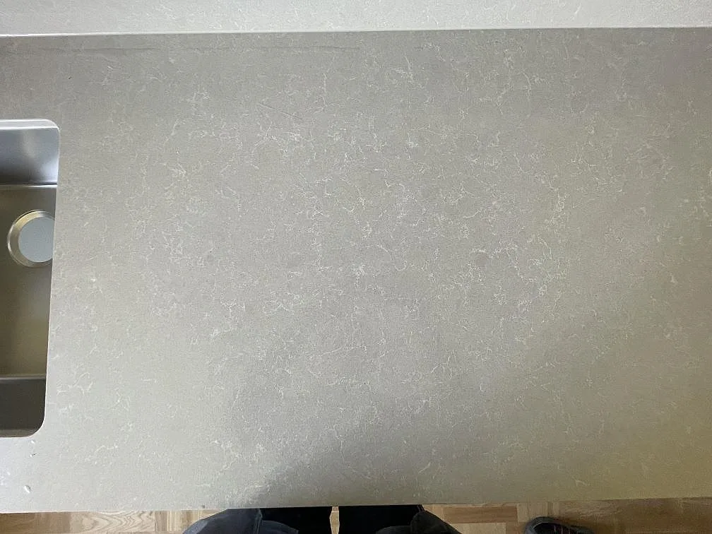 Närbild på ytan av en polerad Technistone Noble Ivory White köksbänkskiva i Sundbyberg som visar den mjuka grå ådringen mot den varmvita botten, intill diskhon.