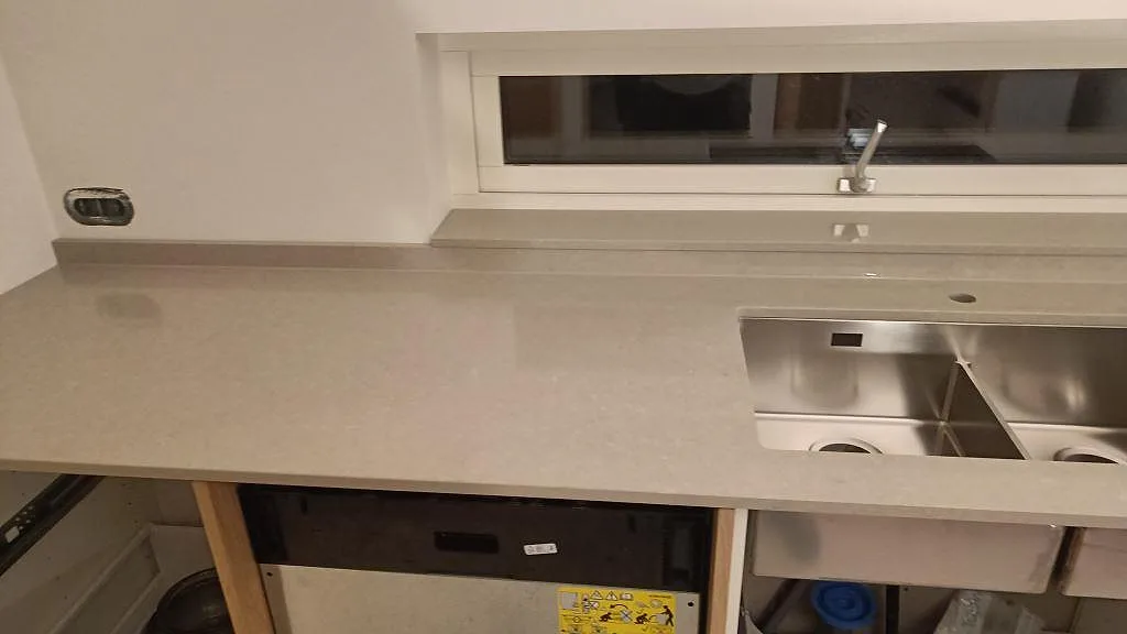 Närbild på polerad Technistone Noble Ivory White bänkskiva med blandarhål, låg stänkkant och diskho vid fönster i Trelleborg.