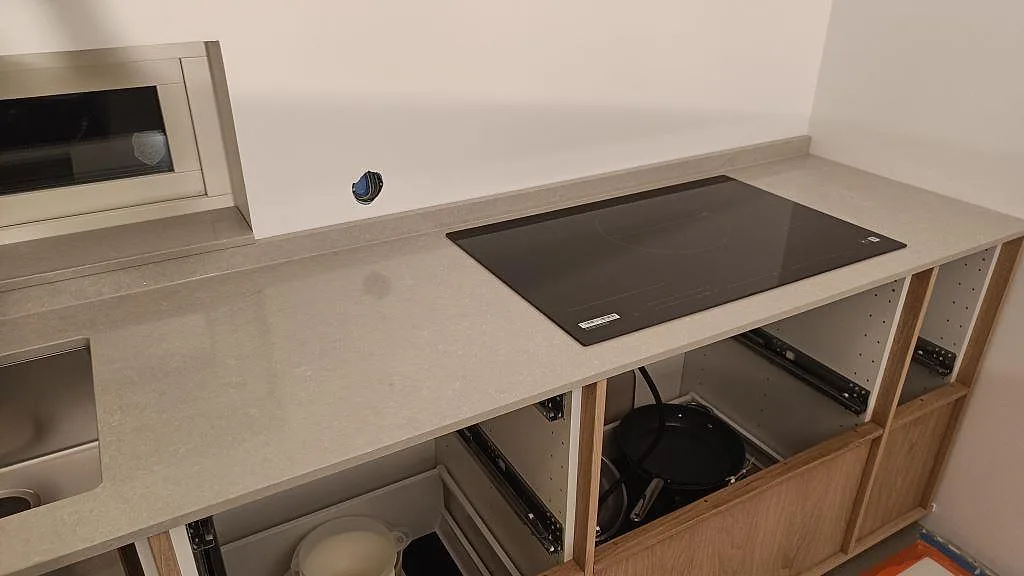 Köksbänkskiva i polerad Technistone Noble Ivory White med hällzon och låg stänkkant i ett kök under montering i Trelleborg.